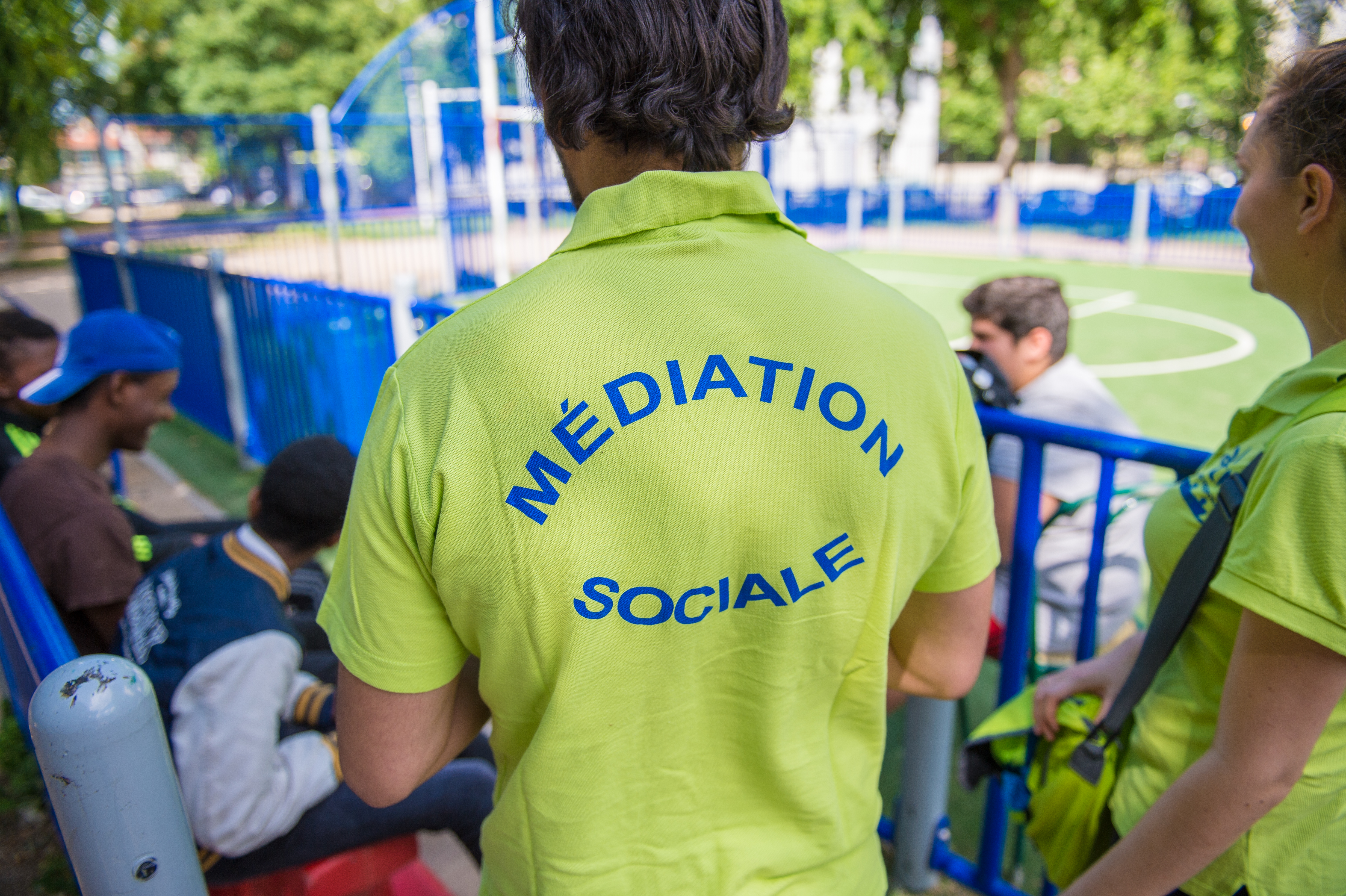 Photo montrant 2 médiateurs sociaux (en t-shirt jaune pour bien les identifiers) en train de parler avec des jeunes sur un banc.