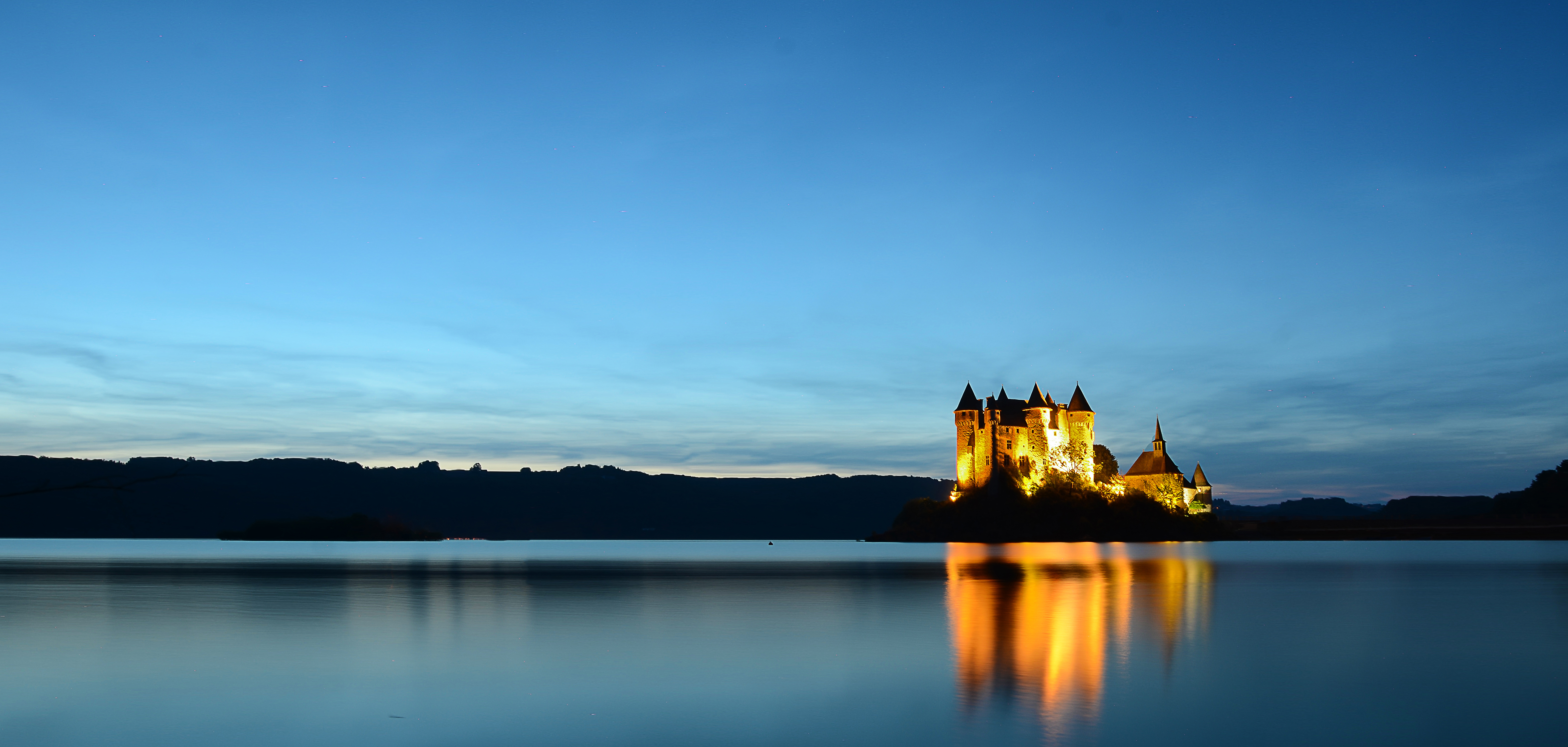 Vue nocturne d'un lac avec un château illuminé qui se reflète dans l'eau