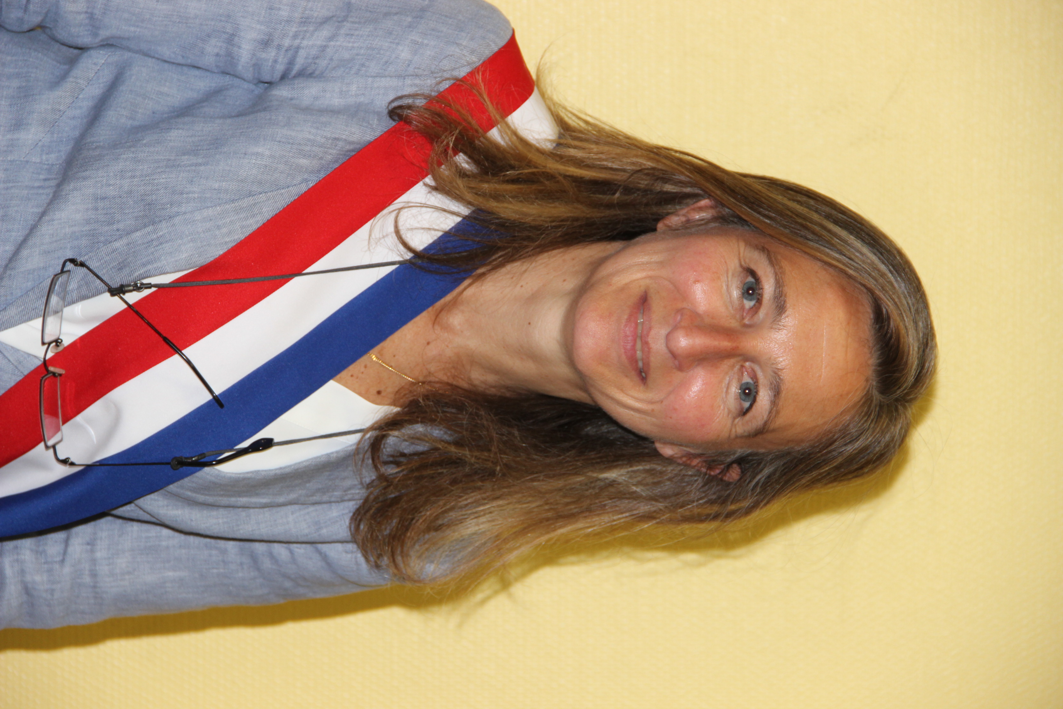 Photo portrait de Mme Galine, cheveux blonds et longs, chemise bleu et écharpe tricolore autour du buste