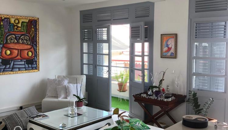 Intérieur d'un appartement rénové : vue du salon depuis la cuisine ouverte et des fenêtres extérieures à clayettes, caractéristiques de la Guadeloupe