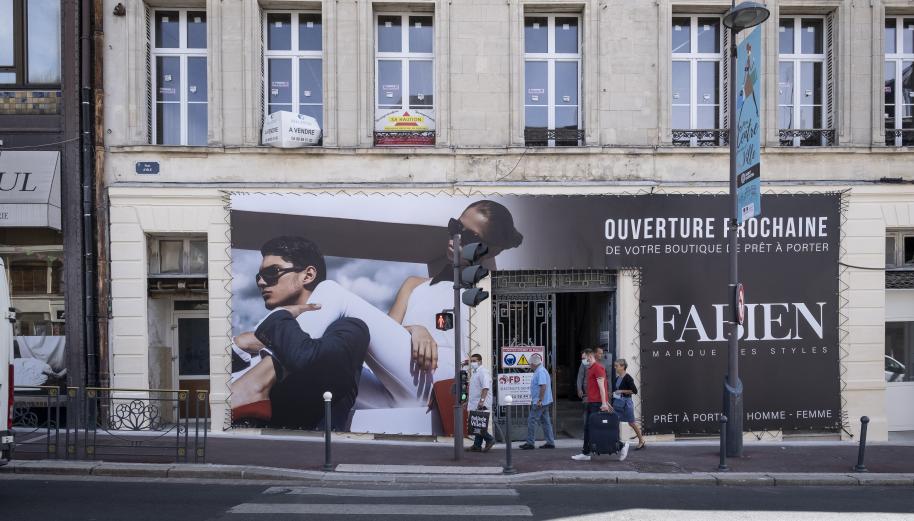 Dans une rue de St-Quentin, dans le Nord, des passants devant une nouvelle boutique qui affiche l'annonce de son ouverture pochaine.
