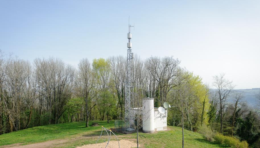 Antenne-relais de téléphonie mobile, entourée d'arbres, de verdure et sous un ciel bleu, sur la colline de la Motte de Vesoul