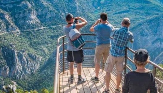 Des touristes en vêtemens d'été sont sur une passerelle de bois qui fait face aux montagnes du Verdon