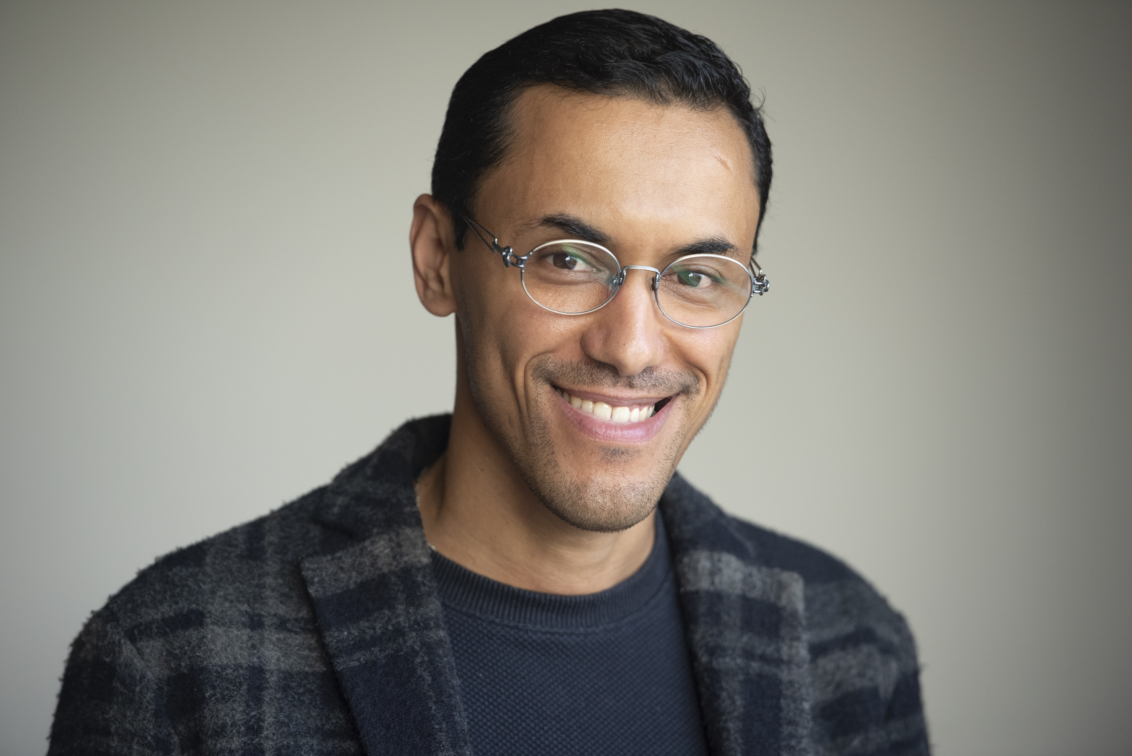 Portrait d'Adil El Ouadehe, souriant, lunette fine, cheveux noirs courts et chemise à carreaux foncée