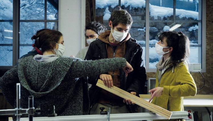 Vue de 3 personnes jeunes dans un atelier, avec une planche en bois