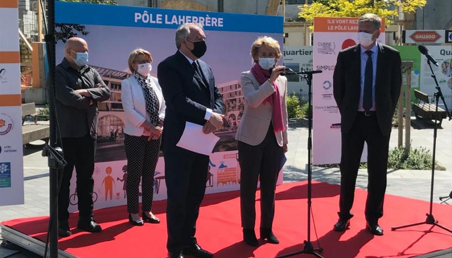 Le maire de Pau, F. Bayrou, et la présidente de l'ANCT, C. Cayeux au micro, sur une estrade rouge pour la pose de la 1re pierre d'un projet immobilier de commerces et habitats.