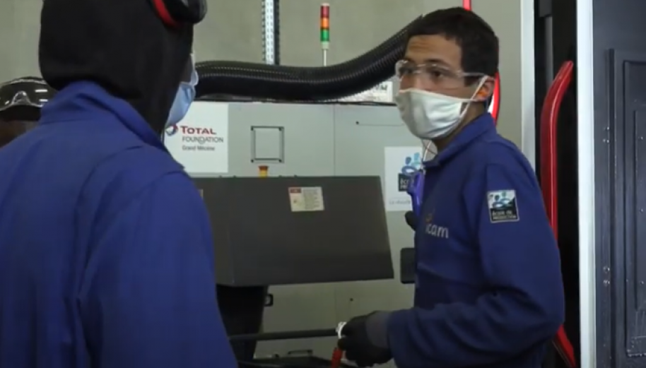 2 jeunes en bleu de travail devant une machine dans une usine